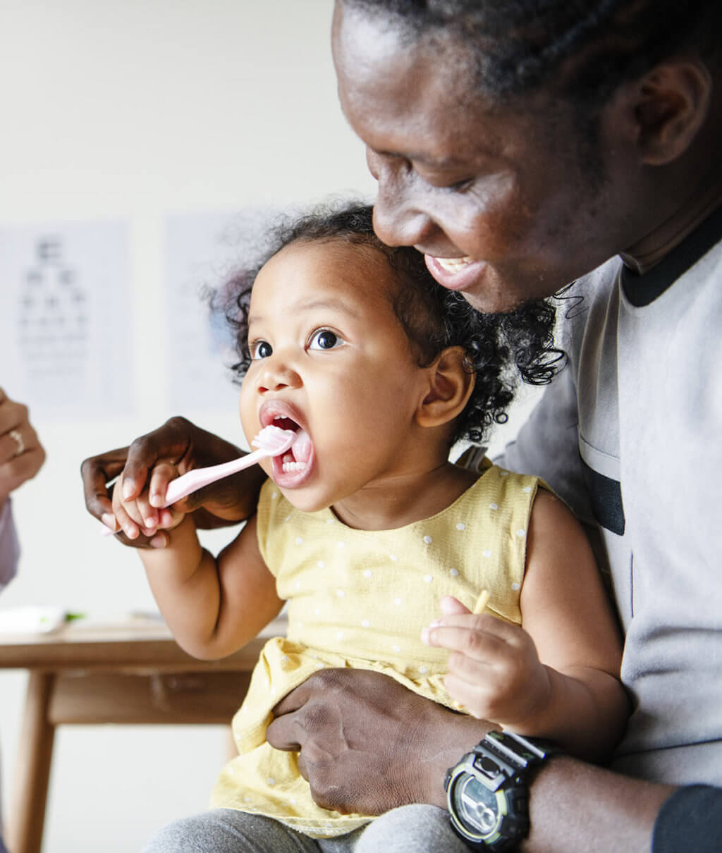 Toddler bushing teeth with father in a dental clinic