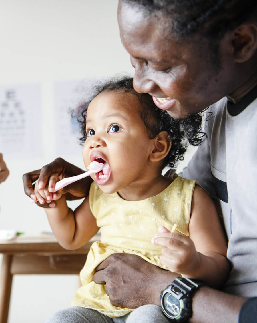 Toddler bushing teeth with father in a dental clinic